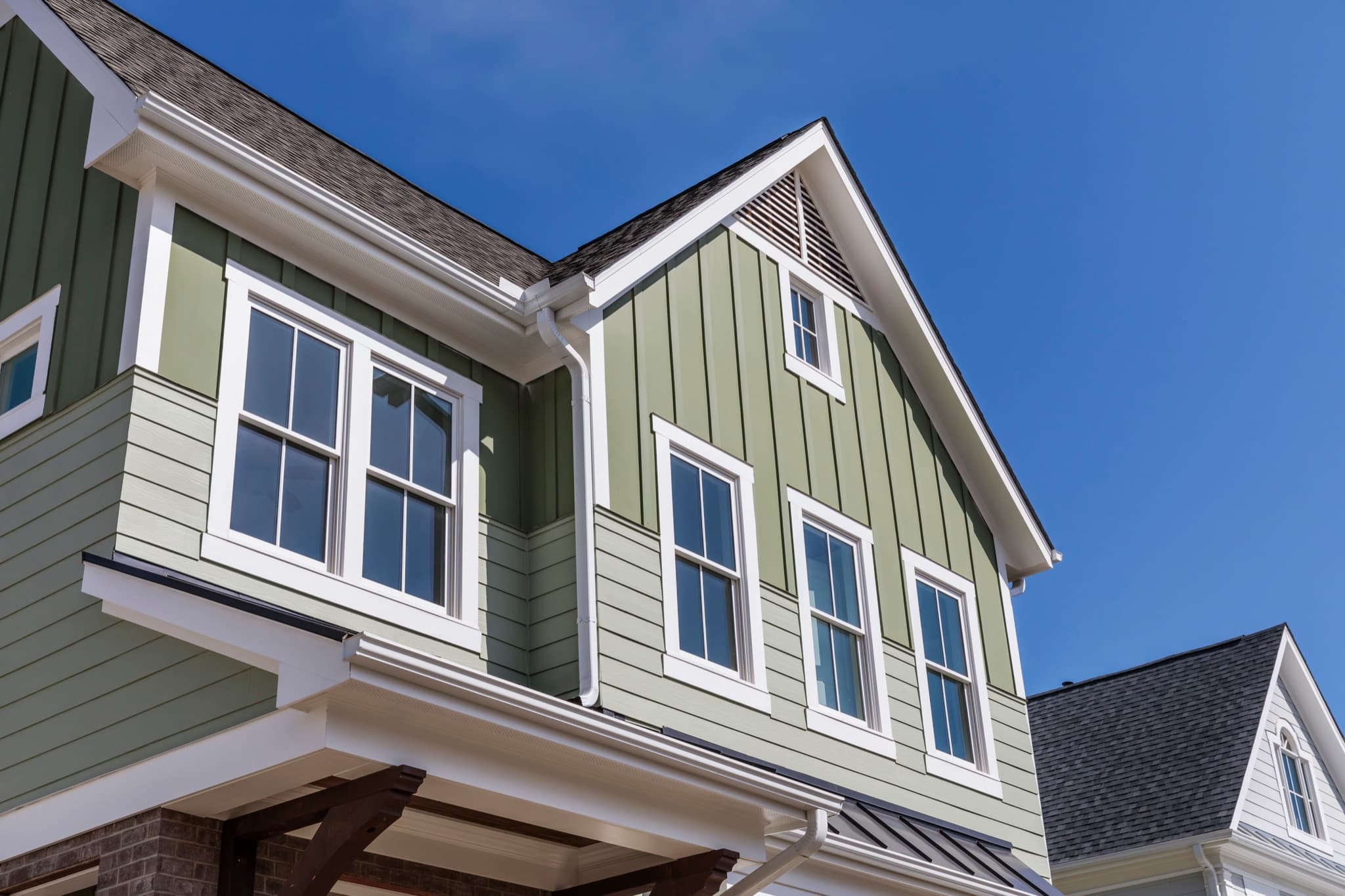 Exterior of a home with new white-trimmed windows and craftsman siding against a blue sky